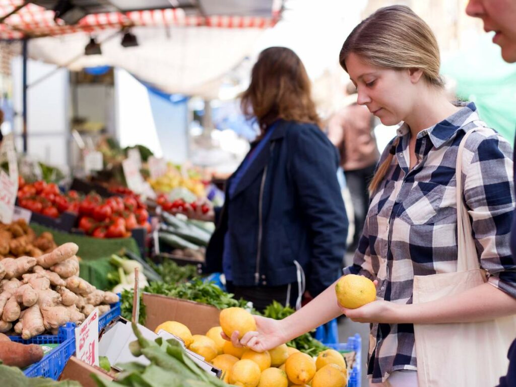 A woman in a checkered shirt selects lemons at an outdoor market.