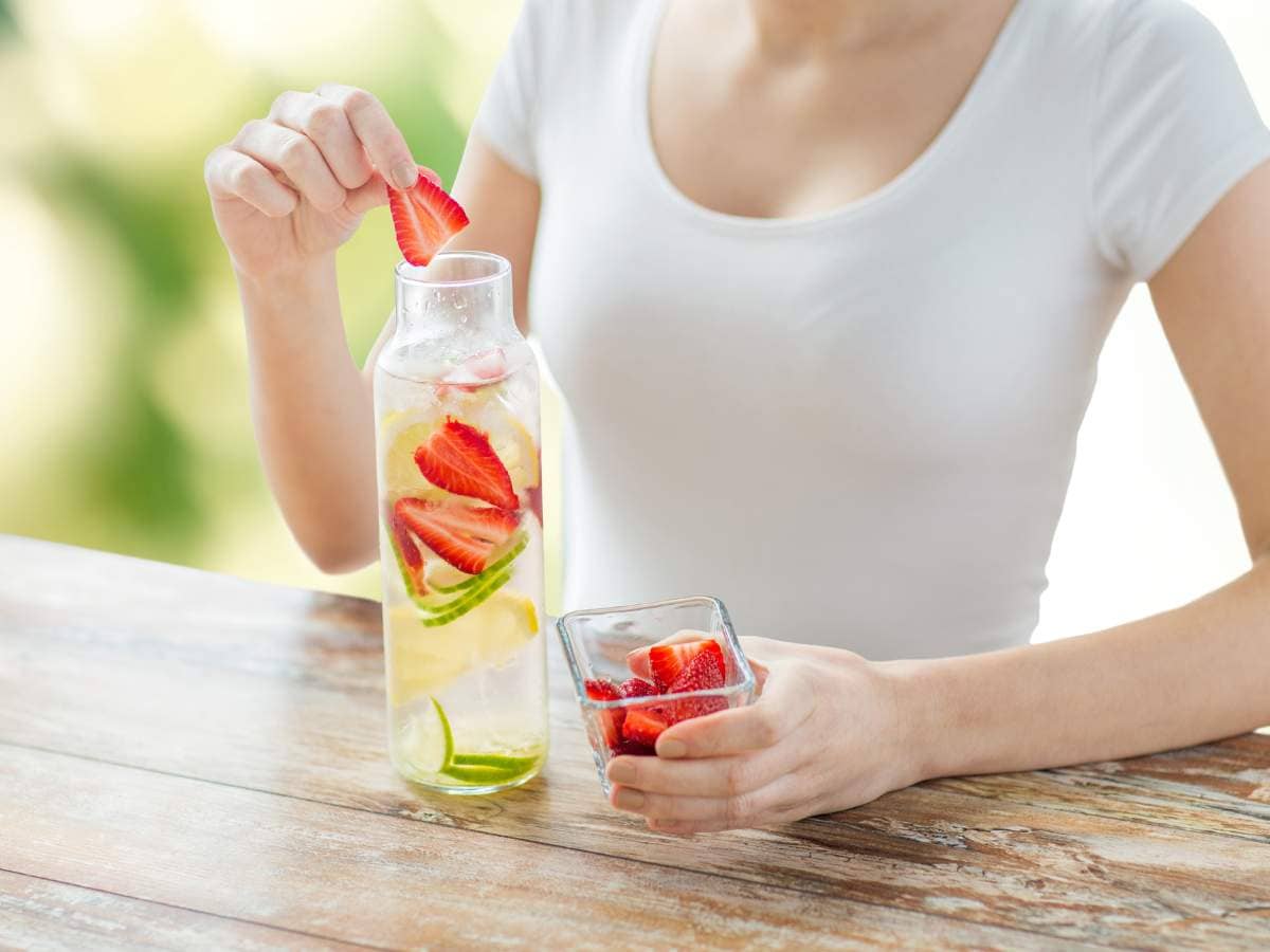 A person in a white shirt prepares a pitcher of infused water by adding sliced strawberries.
