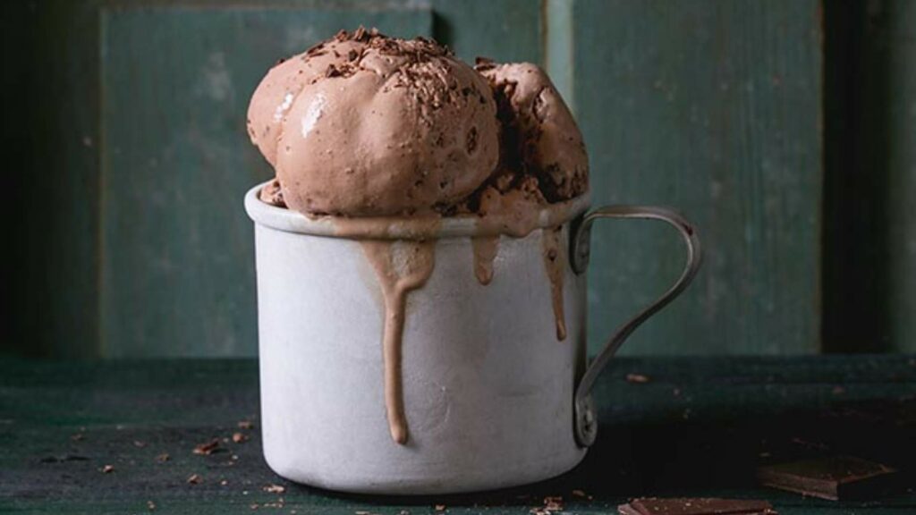 A metal cup filled with scoops of chocolate ice cream, melting over the sides.