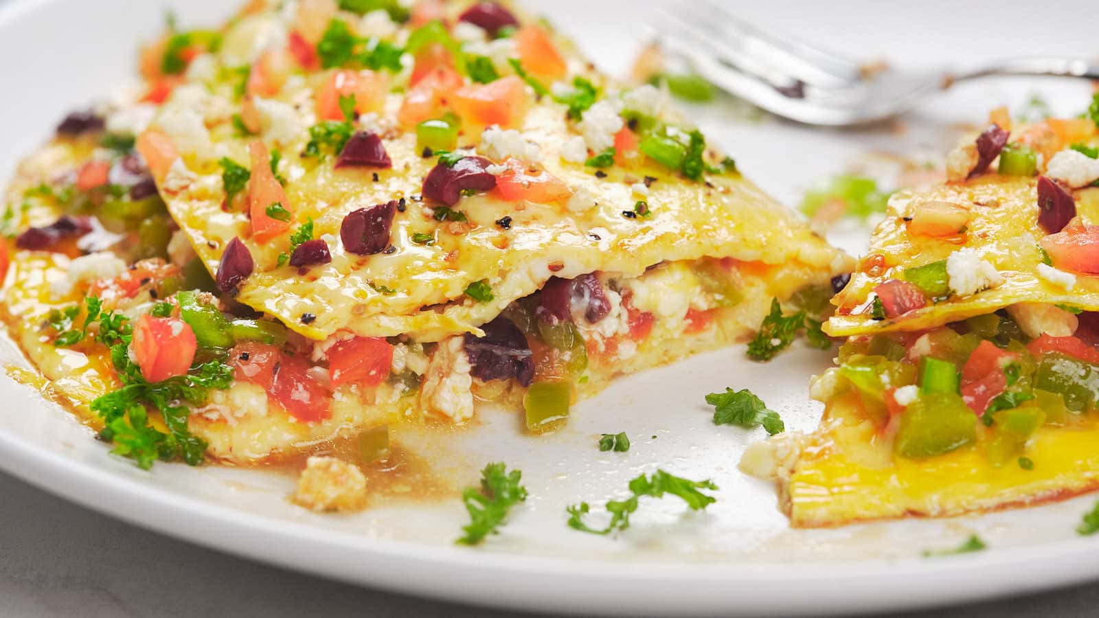 A plated serving of enchiladas filled with various ingredients, topped with fresh chopped vegetables, herbs, and cheese, with a fork beside.