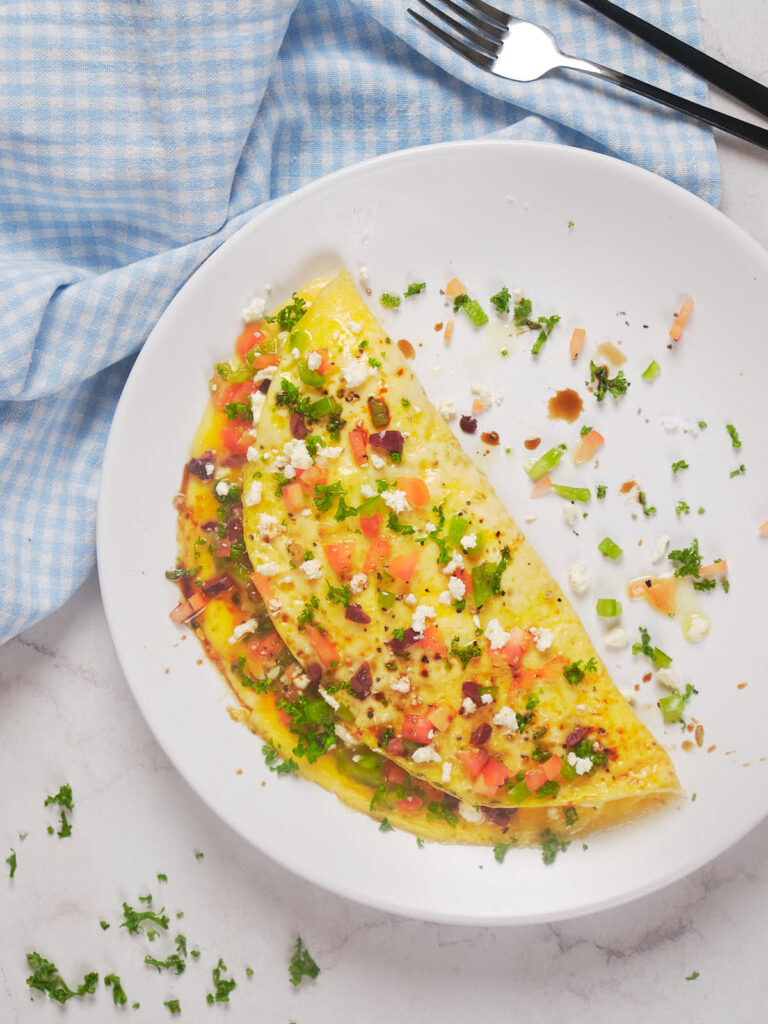 A folded omelet with chopped tomatoes, herbs, and crumbled cheese on a white plate.