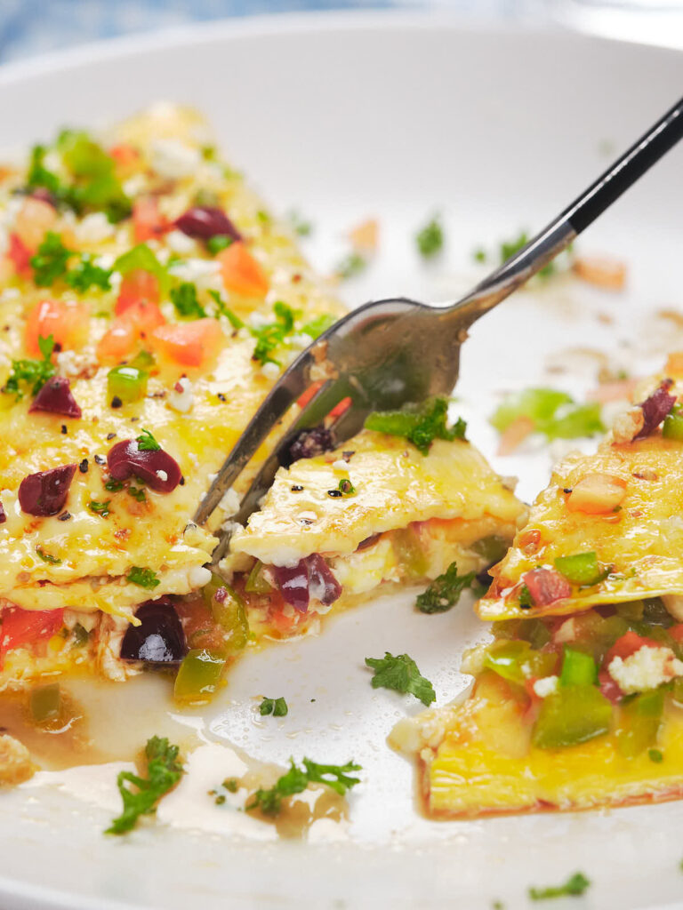 A fork cutting into a colorful vegetable omelet on a white plate.