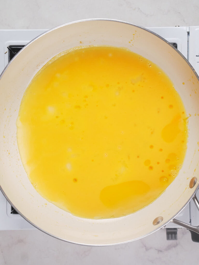 A white pan on a stove contains a yellow liquid that is beginning to cook.