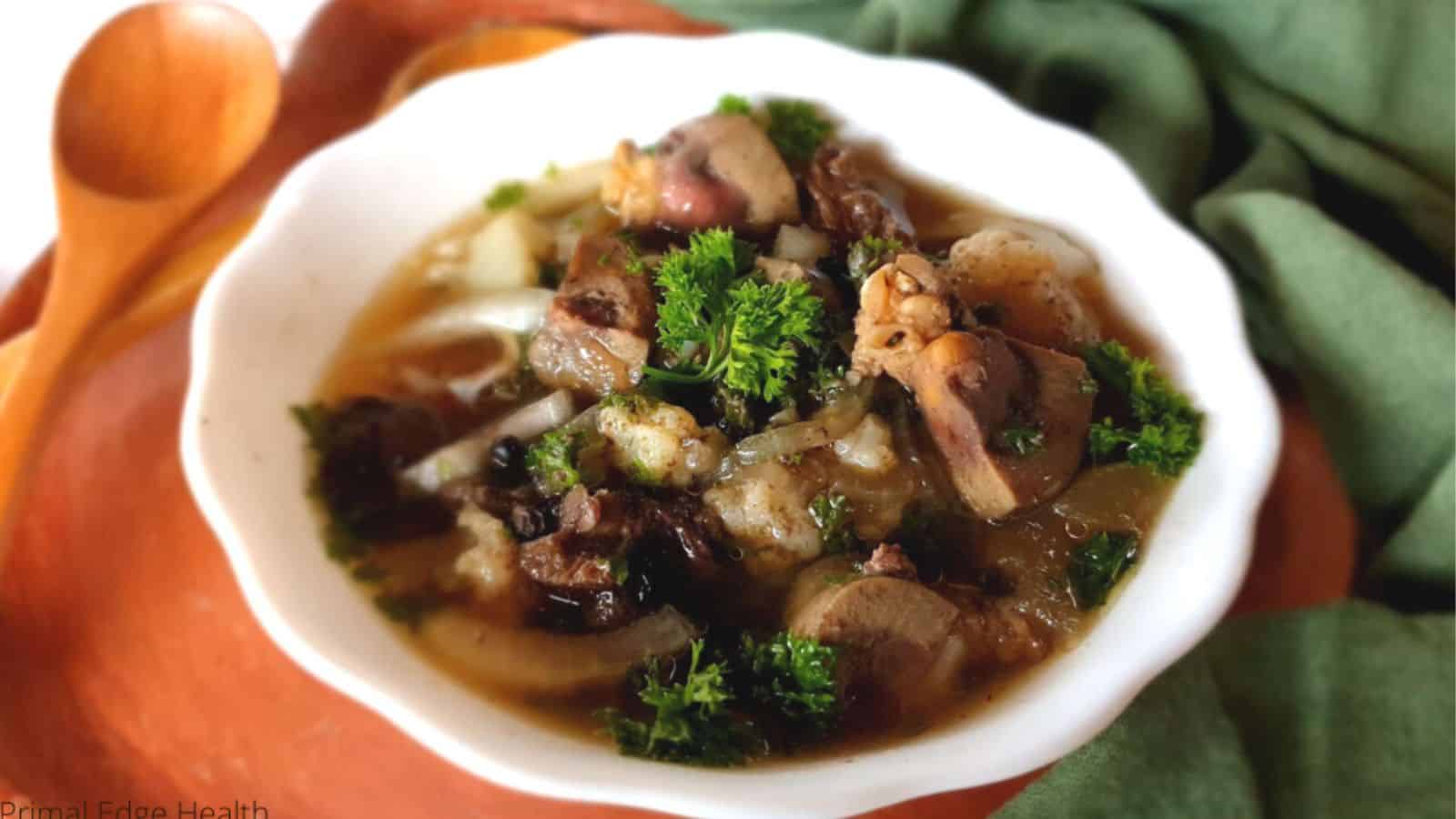 A white bowl filled with a stew featuring pieces of organ meat stew, garnished with fresh parsley.