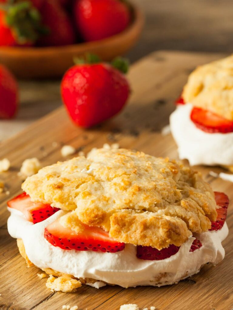 Strawberry shortcake with fresh strawberries and cream between two layers of biscuit on a wooden surface.