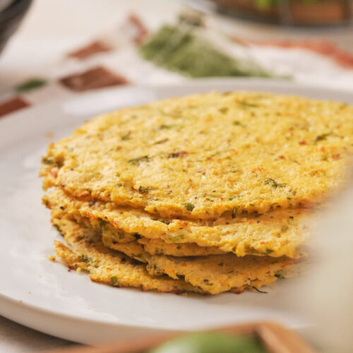 A stack of cooked cauliflower tortilla on a white plate with green herb.