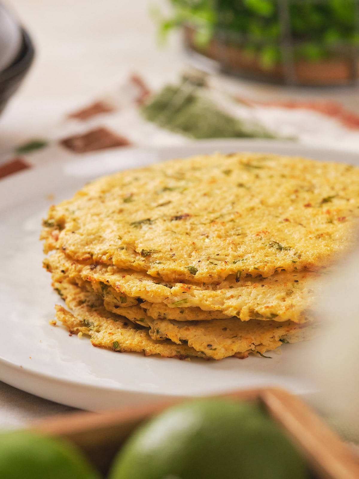 A stack of cooked cauliflower tortilla on a white plate with green herb.