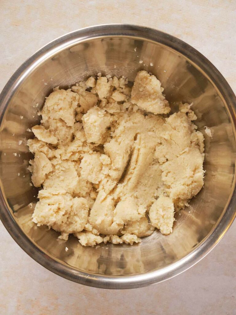 A stainless steel bowl filled mashed cauliflower on a light-colored surface.