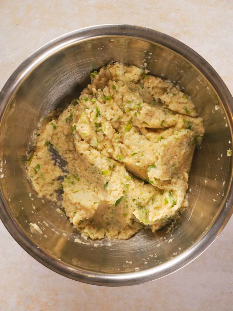 A stainless steel bowl containing a mixture of mashed cauliflower, herbs, and spices, prepared for making tortillas.