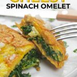 A close-up of a cheesy spinach omelet on a white plate, partially cut with a fork.