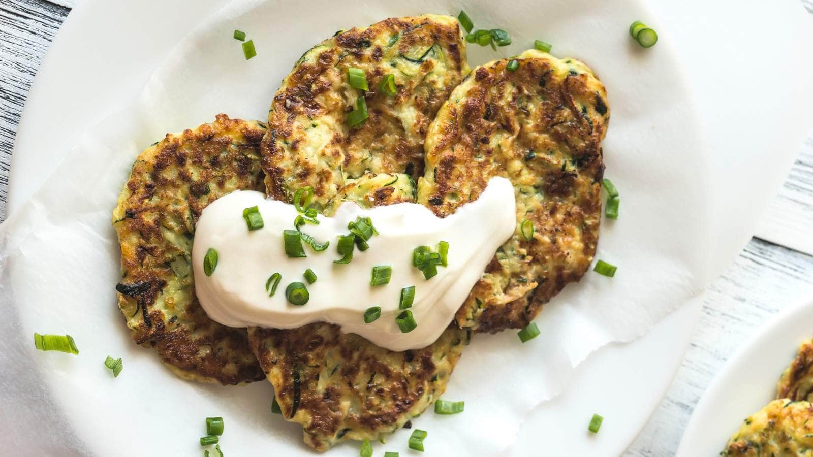 Three pancakes topped with a dollop of cream and garnished with chopped green onions on a white plate.