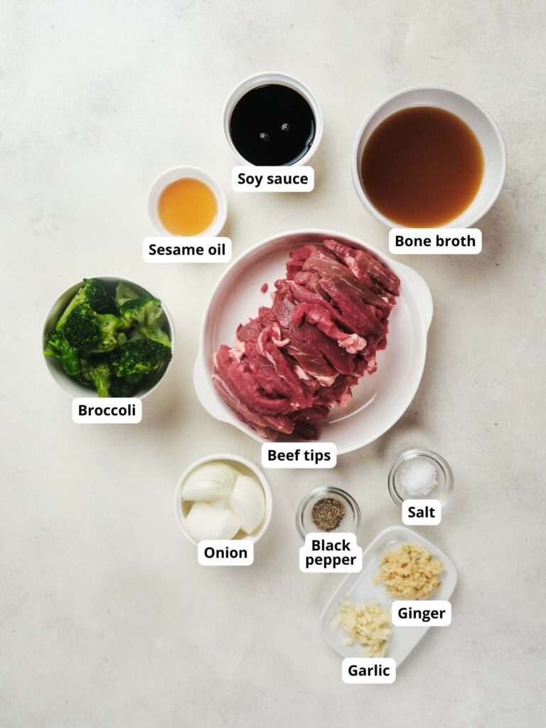 Top-down view of ingredients for a beef stir-fry arranged on a white surface.