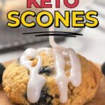 Close-up of a keto scone being drizzled with white icing on a wooden surface.