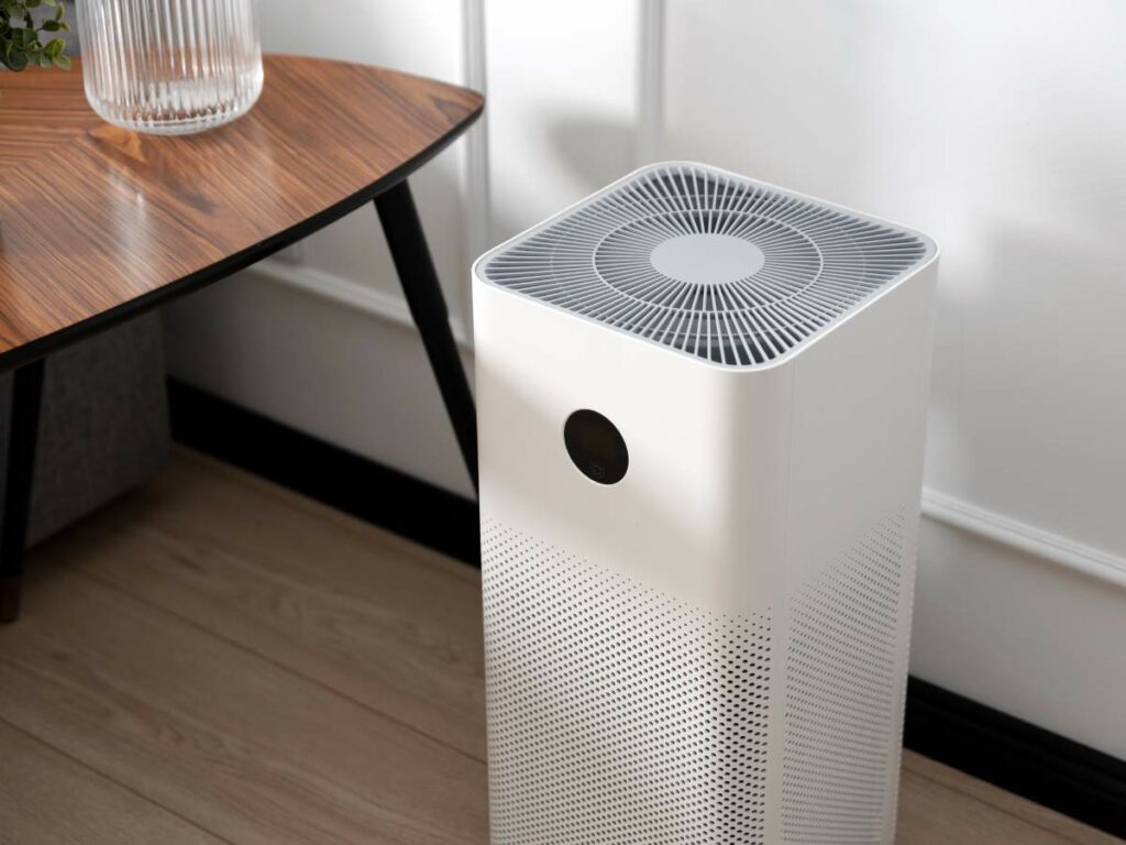 A white air purifier beside a wooden table with a glass vase.