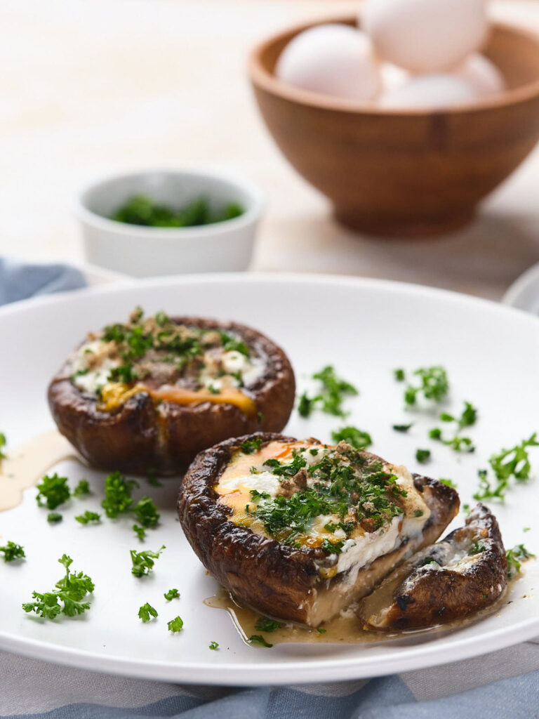 Two egg in mushrooms topped with cheese and herbs on a white plate.