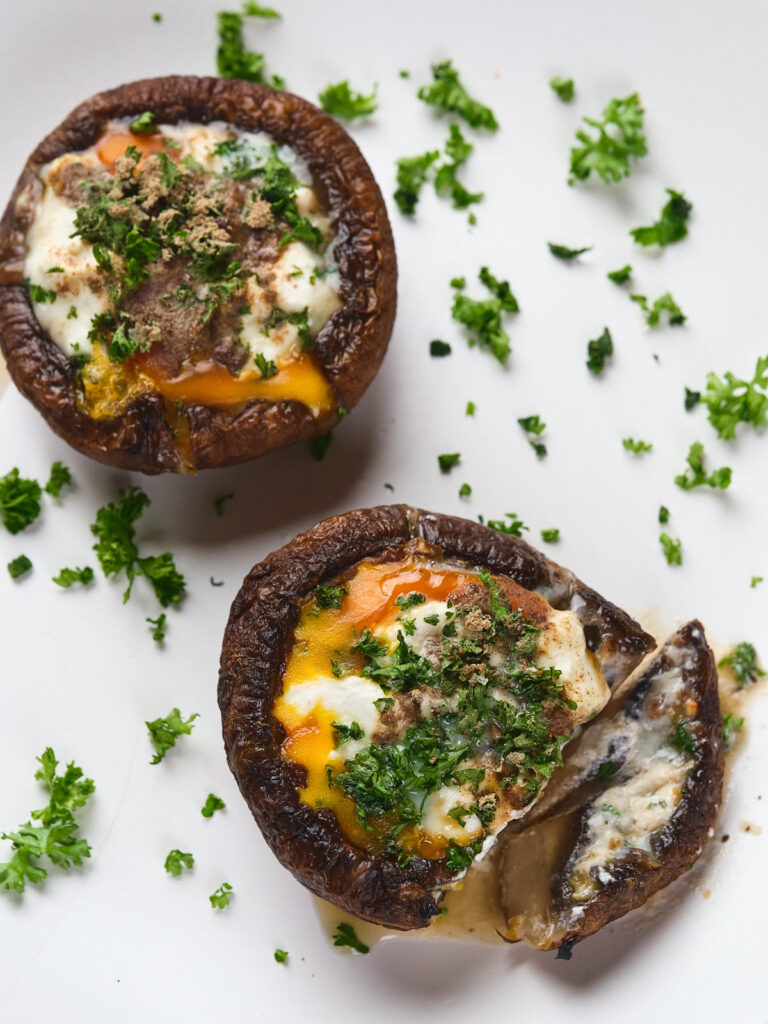 Two egg in mushrooms, set on a white background with scattered parsley pieces.