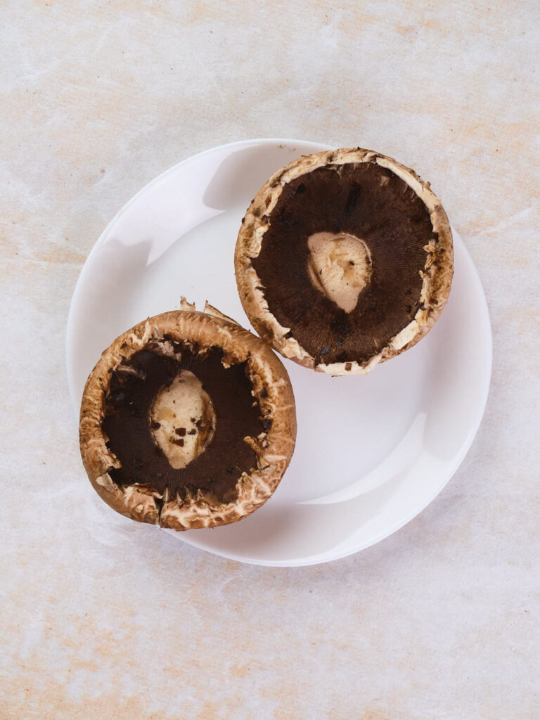 Two whole mushrooms rest on a white plate against a light-colored background.