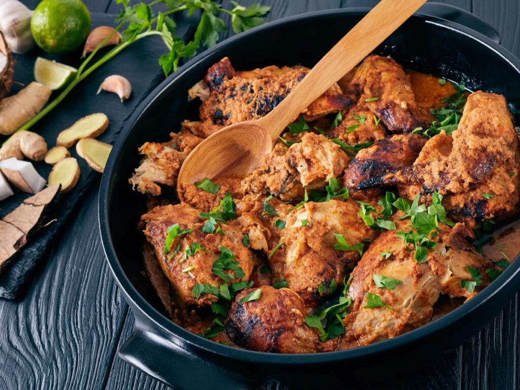 A pan of cooked chicken marinated in a spiced sauce, garnished with fresh herbs.