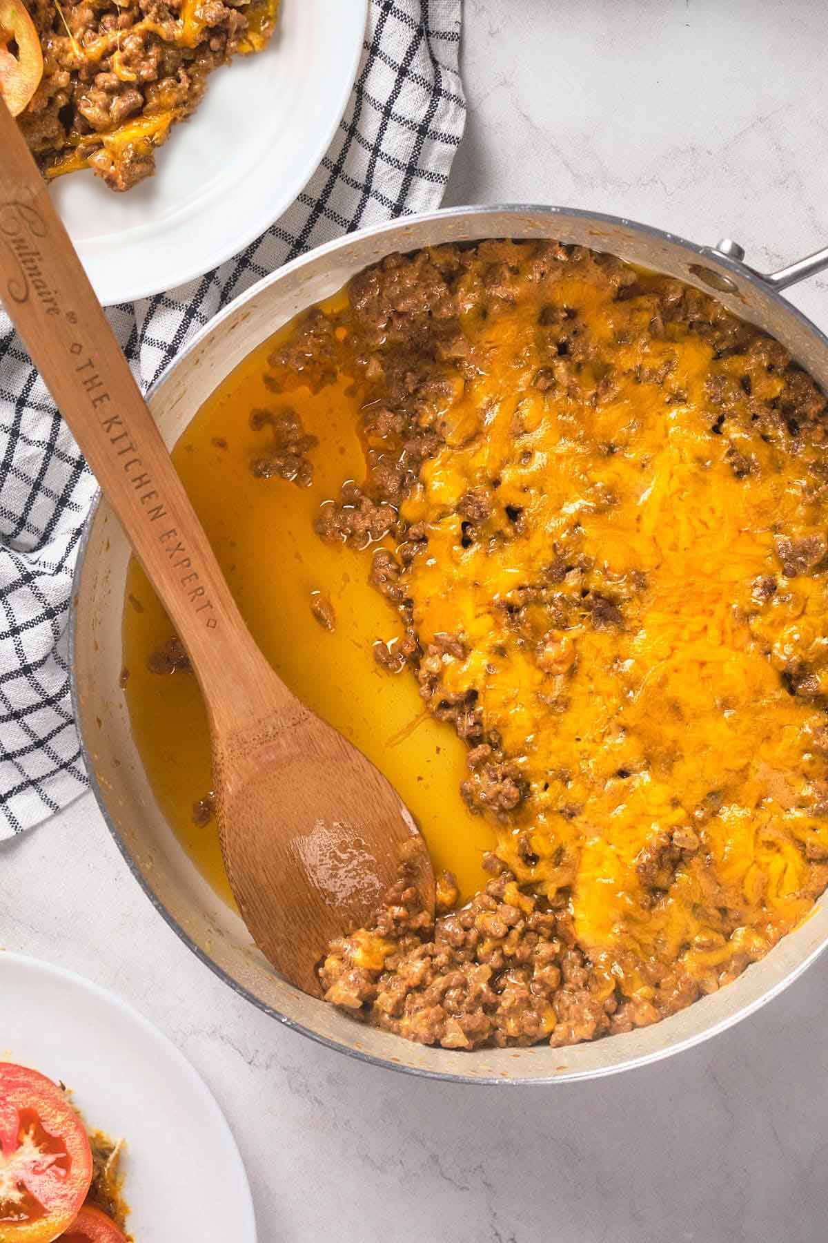 A skillet filled with cooked ground beef topped with melted cheese.