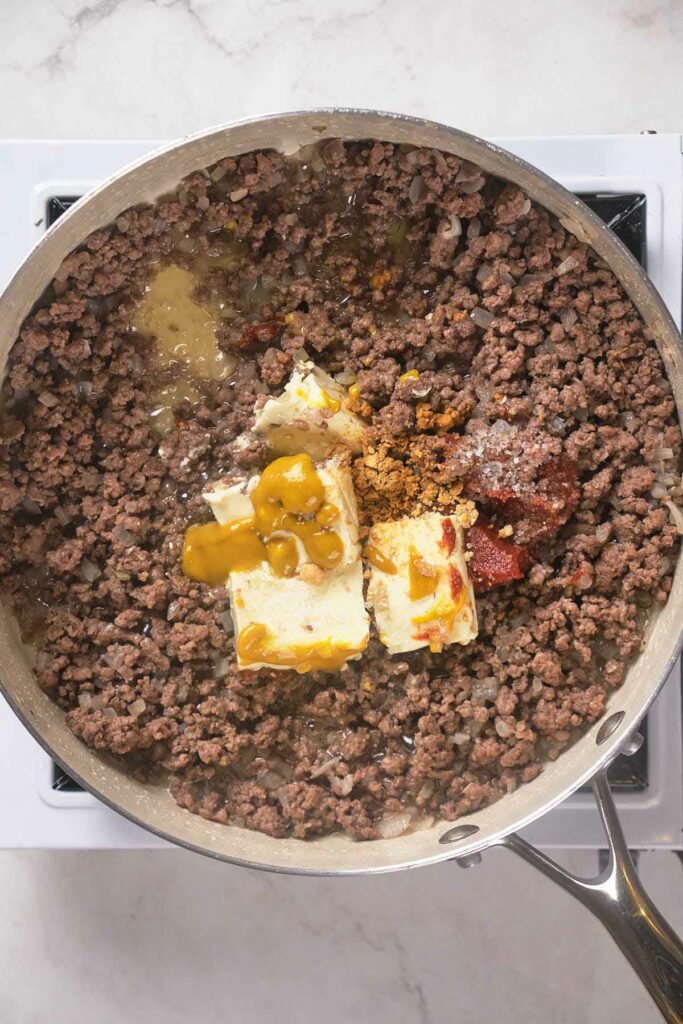 Ground beef cooking in a pan with butter, spices, and sauce on a stovetop.