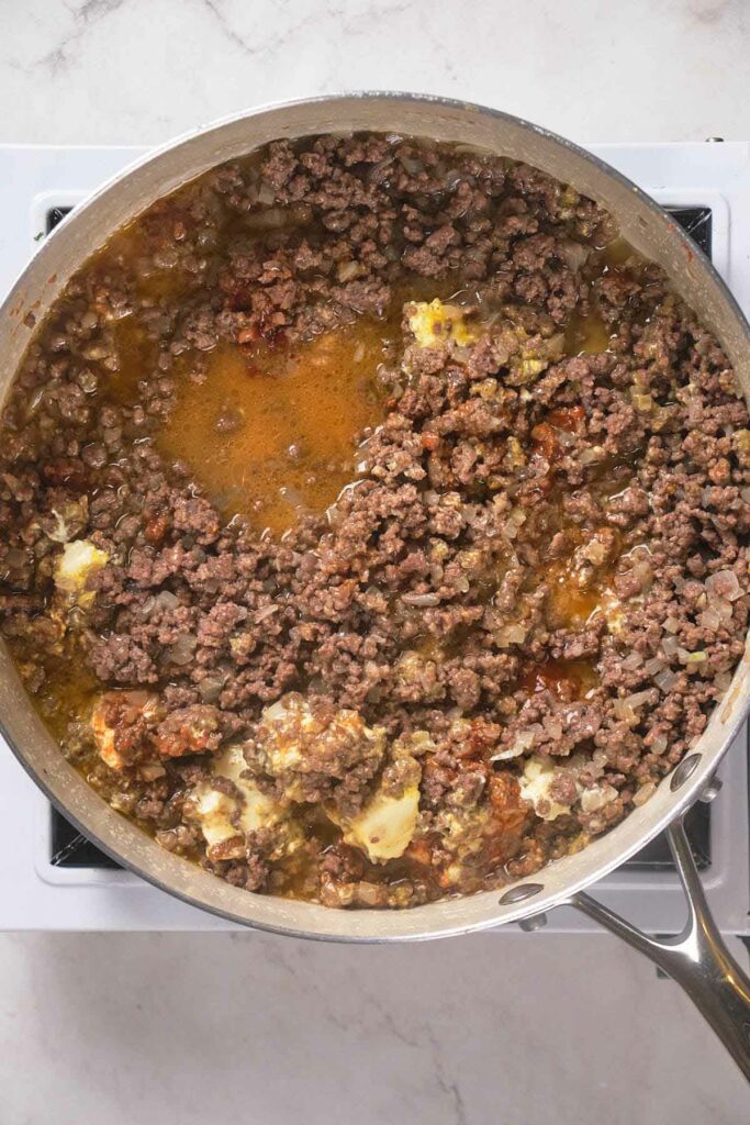 A pan with cooked ground beef, spices, and butter on a stovetop.