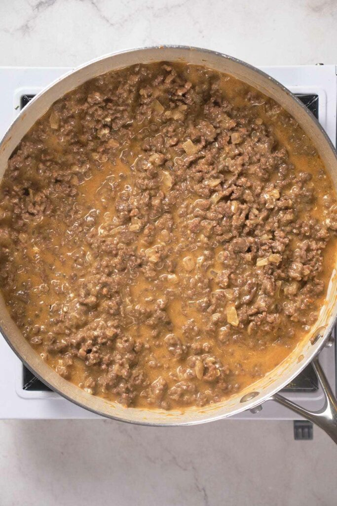 A pan filled with cooked ground beef in a savory sauce on a stovetop.