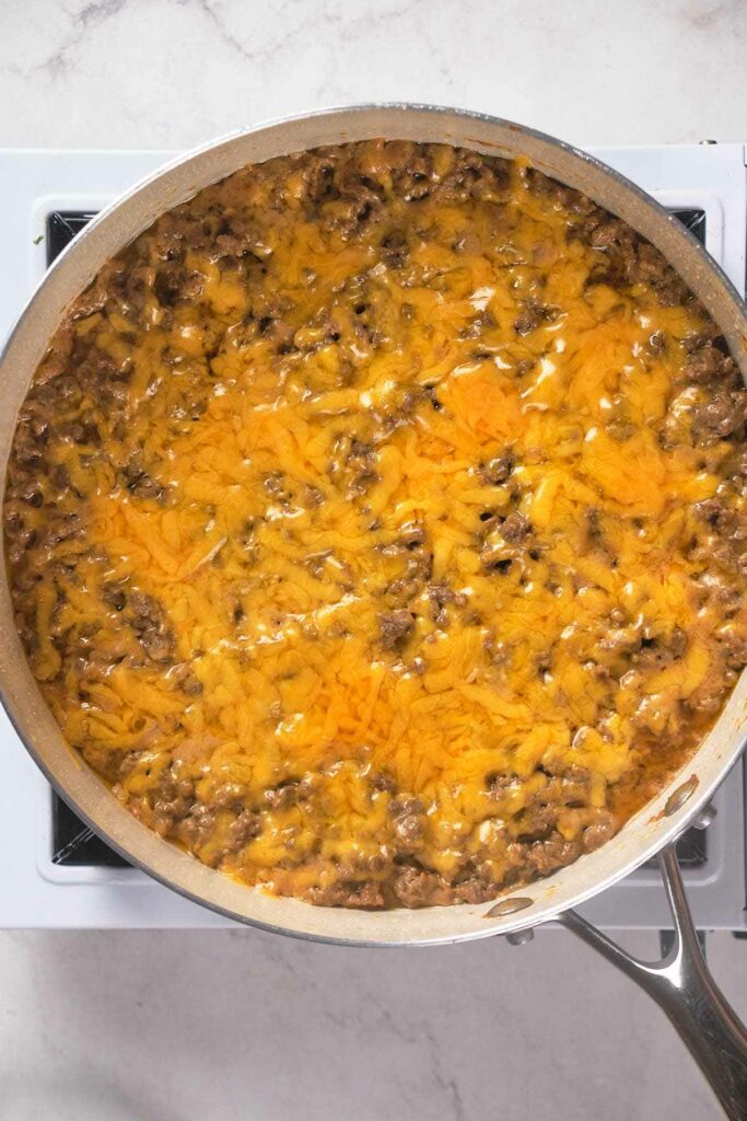 A skillet filled with melted cheese and ground meat atop a stovetop burner.