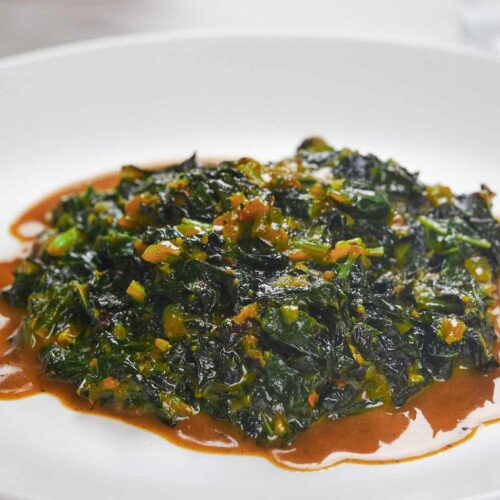 A plate of collard greens with a spicy sauce, served on a white dish.