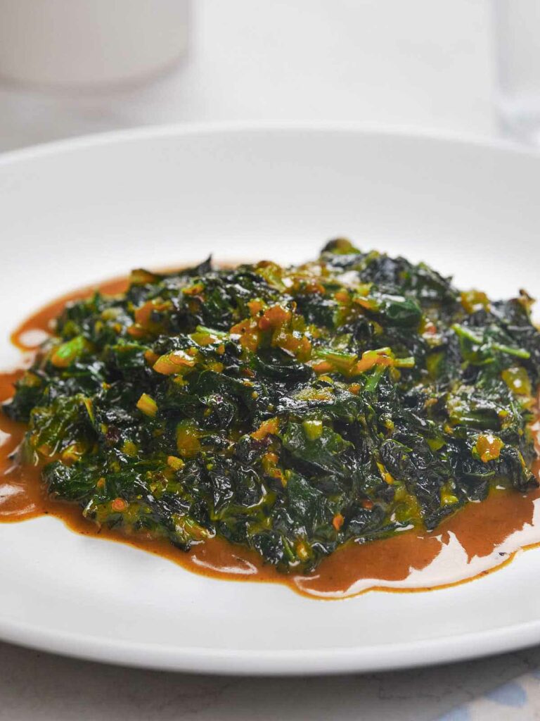 A plate of collard greens with a spicy sauce, served on a white dish.