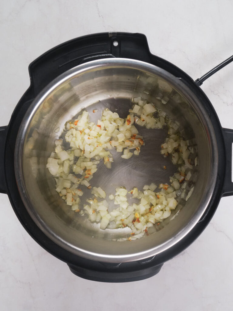 Chopped onions sautéing in an electric pressure cooker on a white surface.