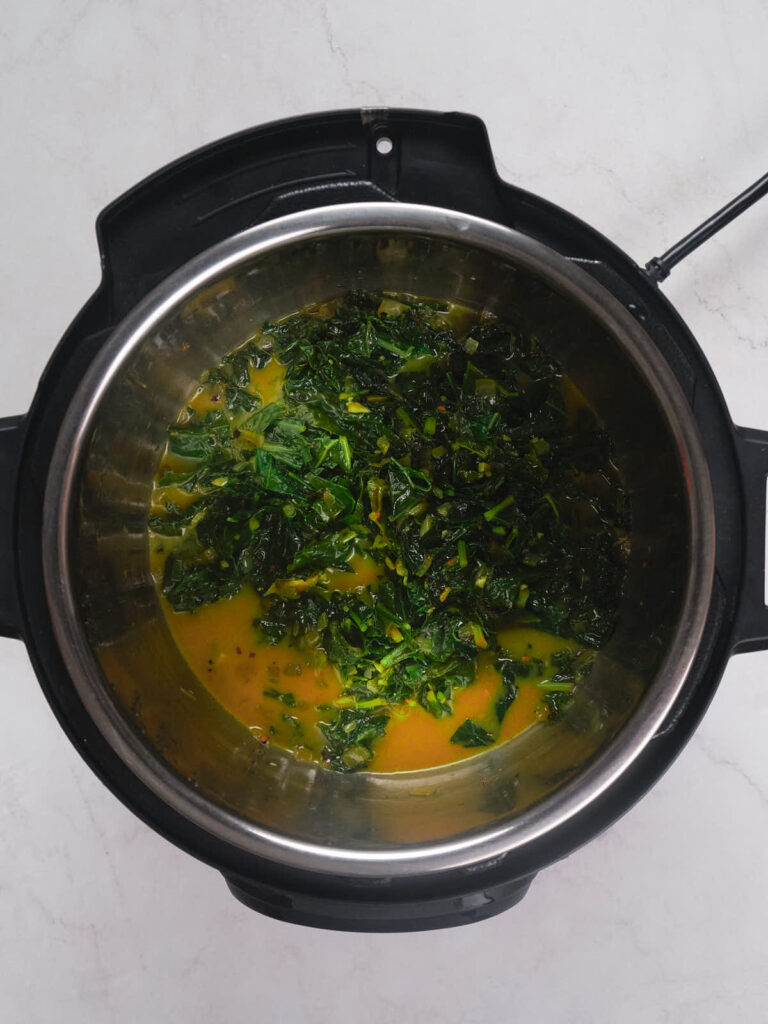 A pot containing cooked greens in liquid, viewed from above. The greens are dark and the liquid is a light orange-yellow color.