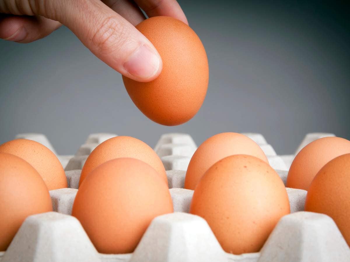 A hand picking up one brown egg from a carton filled with several brown eggs.