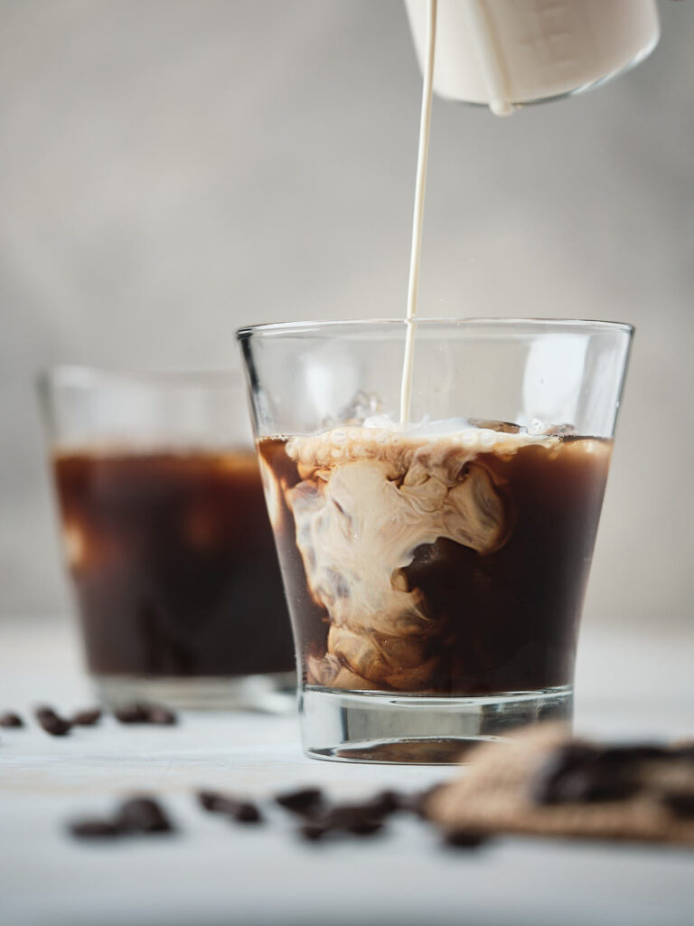 Cream being poured into cold brew black coffee in a glass, creating a swirl effect.