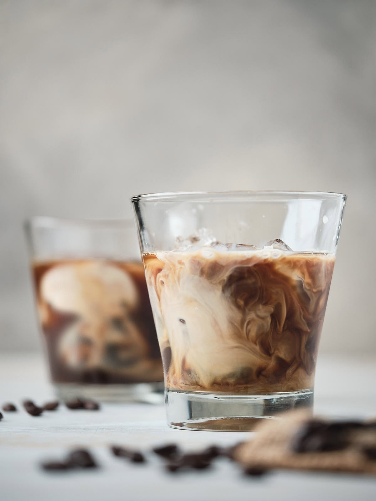 Two glasses of cold brew coffee with milk swirl, placed on a table.