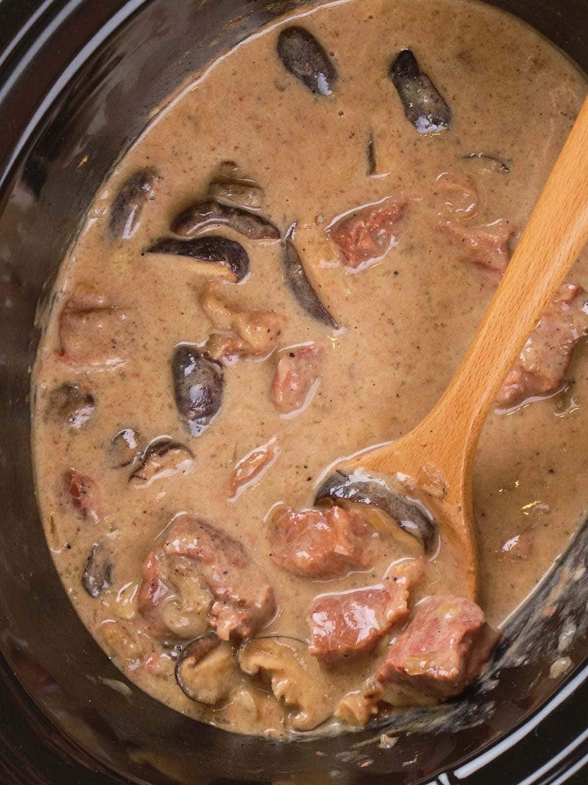 Slow cooker stroganoff with chunks of meat and slices of mushrooms in a creamy brown sauce.