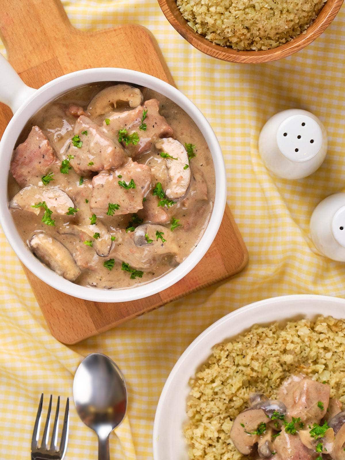 A bowl of creamy slow cooker stroganoff garnished with parsley, served with a side of seasoned rice.