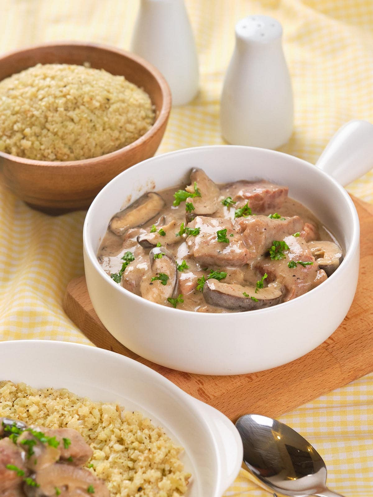 A white bowl of creamy slow cooker stroganoff garnished with parsley, served alongside a bowl.