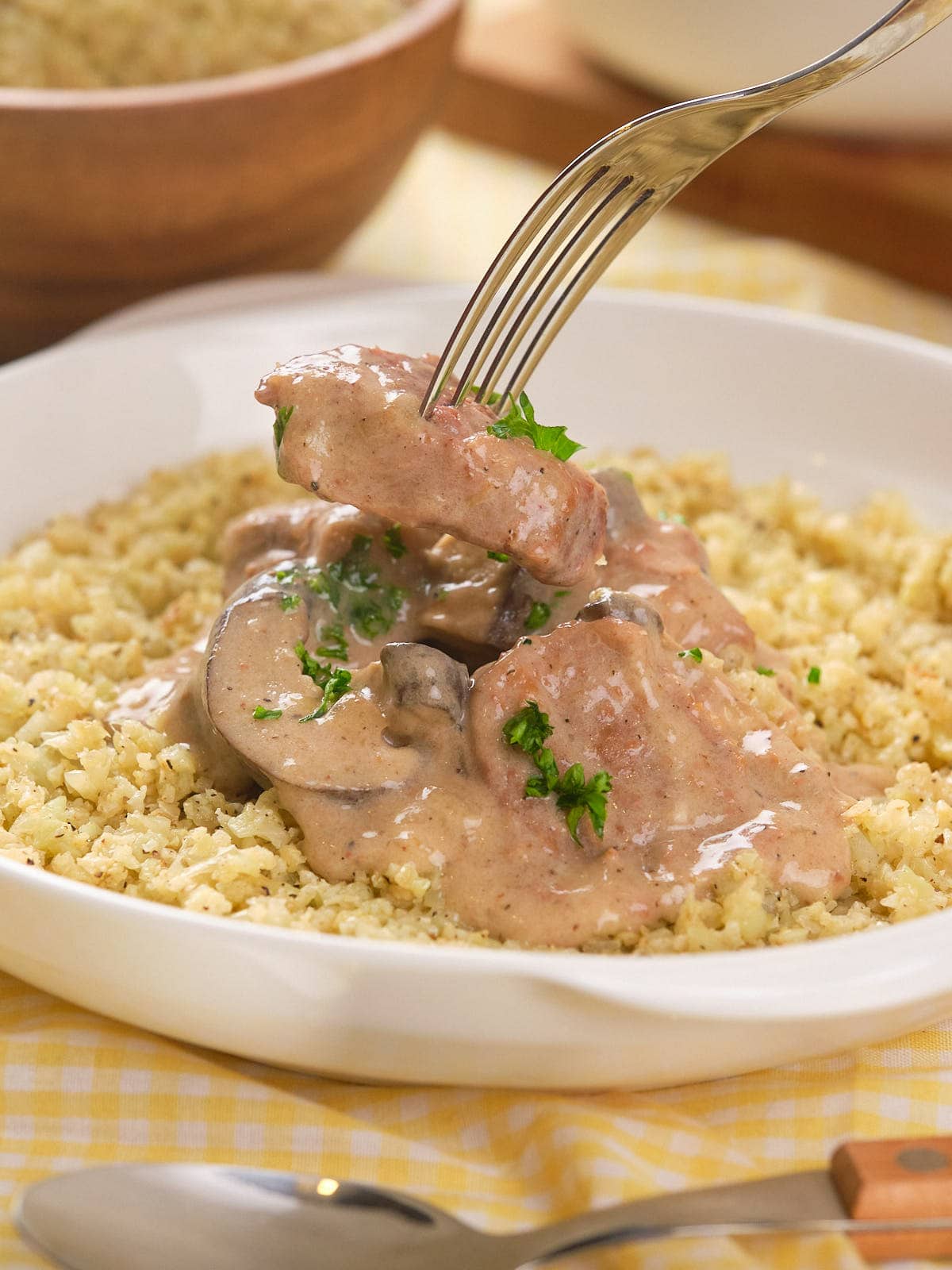 A fork lifts a piece of beef over a plate of creamy slow cooker stroganoff on a white dish.