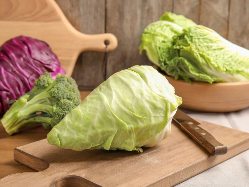 A cabbage sits on a wooden cutting board with a knife.