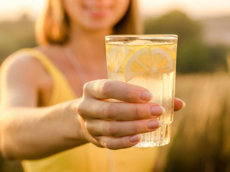 Person holding a glass of lemonade with lemon slices outdoors.