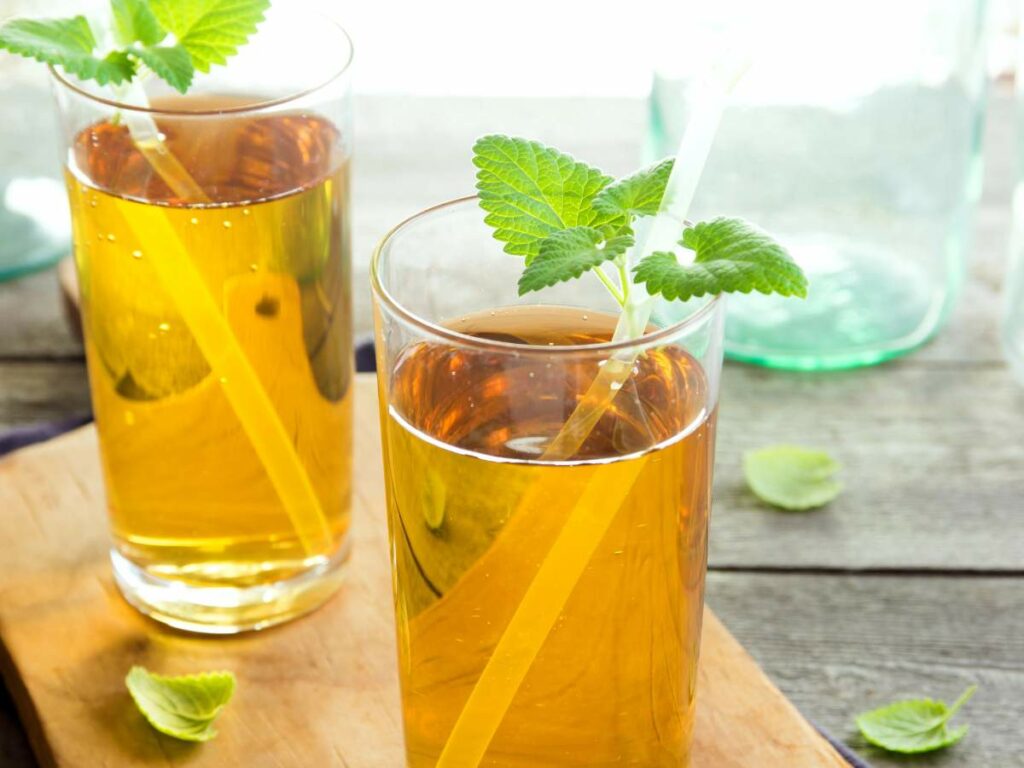 Two glasses of iced tea with lemon slices and mint leaves on a wooden board.