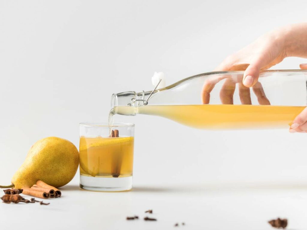 A hand pours apple cider from a glass bottle into a glass.