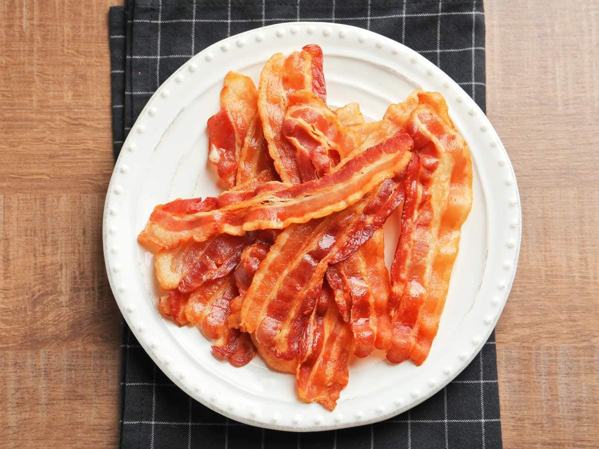 A white plate filled with cooked strips of bacon.