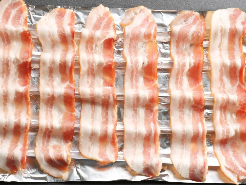 Raw bacon strips laid out on aluminum foil.