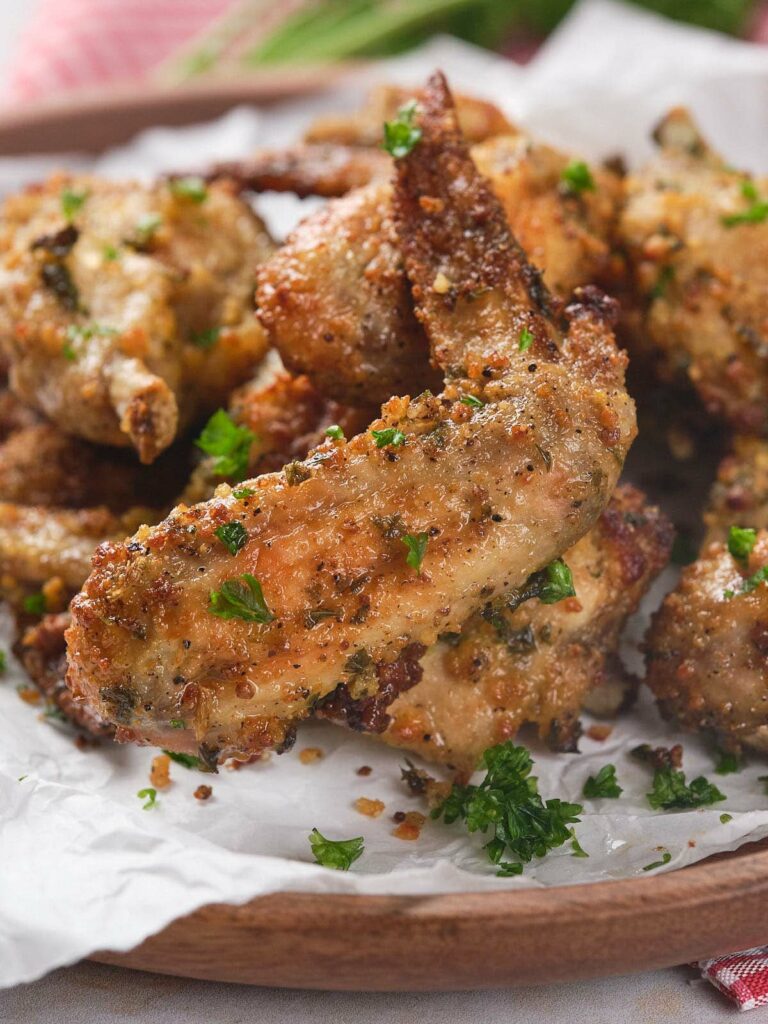 Parmesan chicken wings arranged on a wooden plate lined with parchment paper.