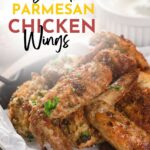 A plate of parmesan chicken wings on parchment paper, next to a bowl of dipping sauce.