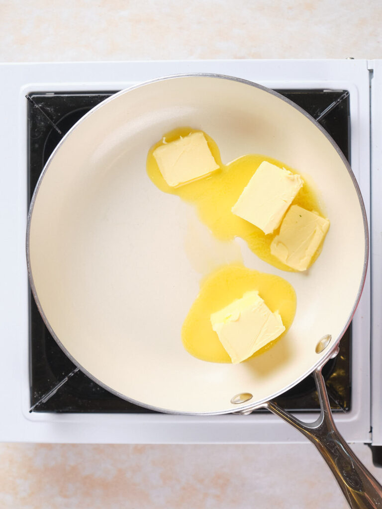 Butter melting in a frying pan on a stovetop.