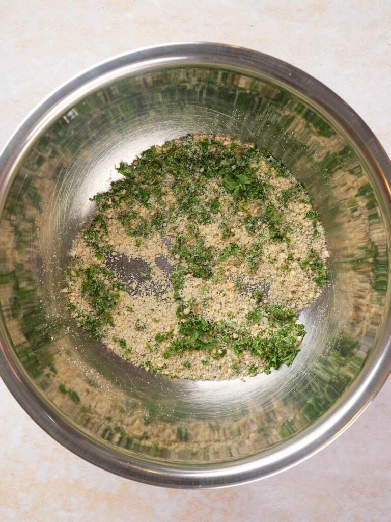 A metal mixing bowl containing cheese and chopped herbs.