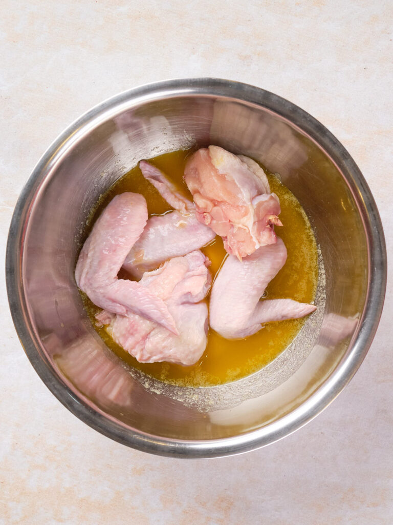 Raw chicken wings in a stainless steel bowl with melted butter.