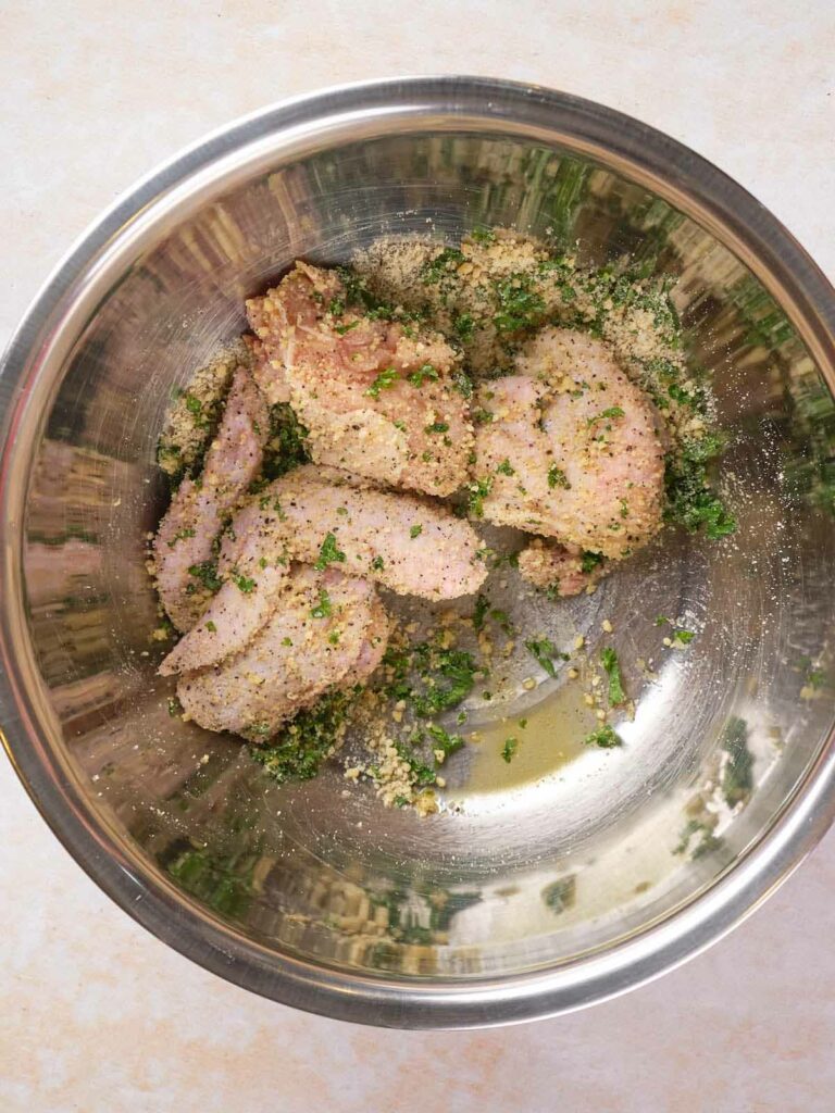 Raw chicken breasts seasoned with herbs and cheese in a metal bowl.